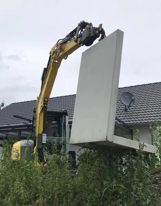 Ein Bagger hieft eine schwere Betonplatte an den richtigen Platz